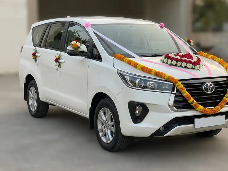White Toyota Innova Crysta decorated with marigold garlands and pink ribbon for a wedding in Ahmedabad